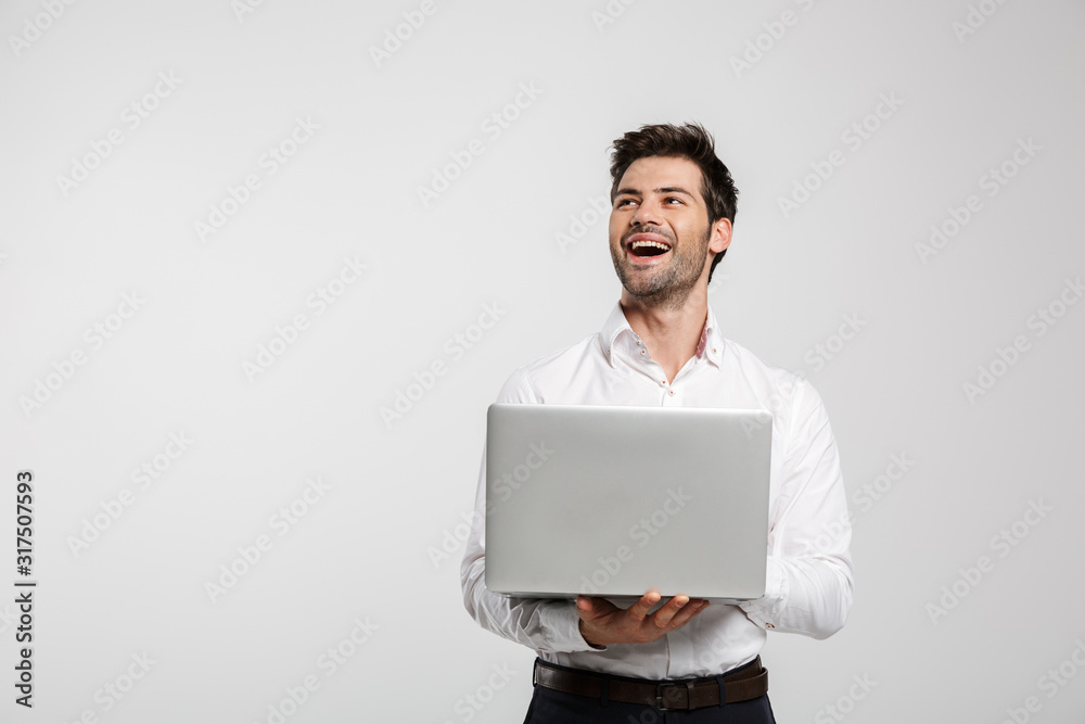 Image of young laughing businessman holding and using laptop - obrazy, fototapety, plakaty 