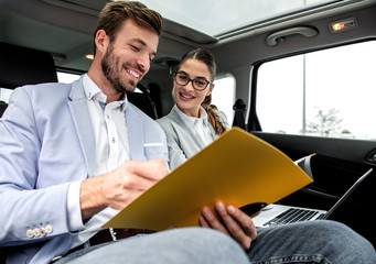 Wall Mural - Young business people working together while traveling by a car. They are using laptop and preparing for meeting.	