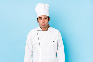 Wall Mural - Young cook man isolated shrugs shoulders and open eyes confused.