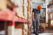 © standret - Young male worker in uniform is in the warehouse pushing pallet truck