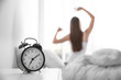 © New Africa - Young woman stretching at home in morning, focus on alarm clock