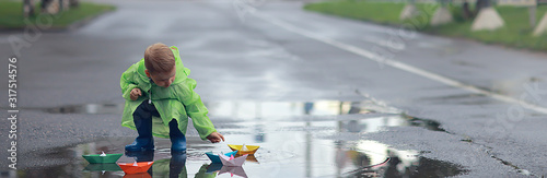 Fotografía a boy plays boats in a puddle / childhood, walk, autumn game in the park, a chil