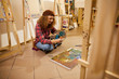© IVASHstudio - Curly girl sits on a floor and draw a painting with oils