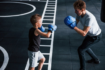 Young trainer teaches kid boxing sport in the gym