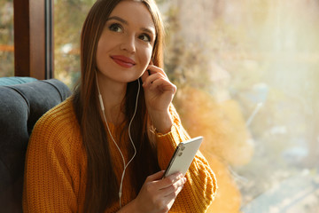 Wall Mural - Woman listening to audiobook near window in cafe