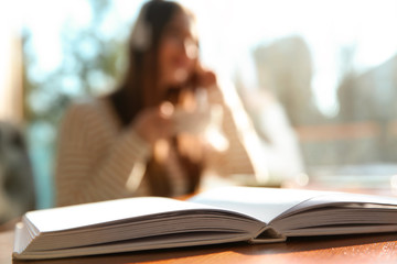 Wall Mural - Book on table in cafe and woman with headphones on background. Audiobook concept