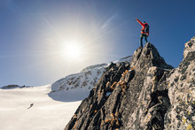 Climber Or Alpinist At The Top Of A Mountain. A Success Of Mountaineer Reaching The Summit. Outdoor Adventure Sports In Winter Alpine Moutain Landscape. Sunny Day And A Climber On A Top Of A Peak.