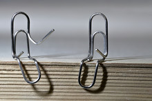 Two Paper Clips In The Form Of Men Sit On A Stack Of Paper. Macro Mode.