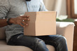 © fizkes - Close up view carton box on african guy lap indoors