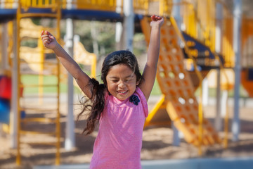 a cute latino girl jumping with joy as she plays in a kids playground.