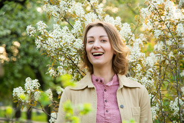 Wall Mural - Portrait of a beautiful happy young woman on the background of a spring blooming tree garden