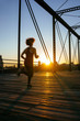 Woman in fitness attire running on pedestrian bridge in city at sunset