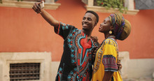 African Young Happy And Good Looking Man And Woman In Traditional Clothes Standing Together Outdoor And Taking Selfie Photos On The Smartphone Camera.