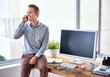 © marvent - Businessman on his phone sitting on the edge of his desk