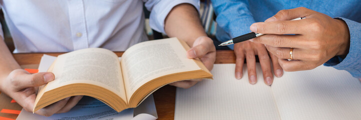 tutor and college students teaching school work and explaining problem solution studying and reading together in a table at class room.