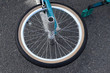 Bicycle wheel with teal fork and pedal on grey pavement