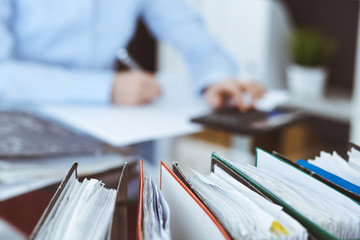 Binders of papers waiting to process by bookkeeper woman or financial inspector, close-up. Business portrait. Audit or tax concepts