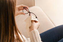 Young Woman Wiping Eyeglasses At Home, Closeup