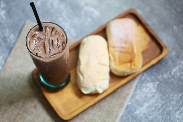 Poster - Ice chocolate fresh drink in the glass with sweet cream breads on wood tray put on stone background 