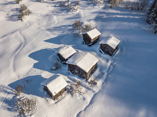 Wall Mural - Aerial view of snow covered cottages in wild rural countryside. Tranquil scene with beautiful wooden houses in remote mountain area.