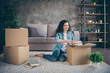 © deagreez - Nice attractive lovely cheerful cheery wavy-haired girl sitting on floor carpet opening unwrapping unpacking her own things in modern loft industrial style interior living-room