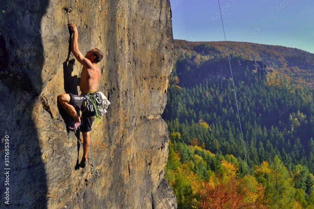 Young man is climbing on the sandstone rock in Sachsen Switzerland. Beautiful autumn day in Germany. - obrazy, fototapety, plakaty 