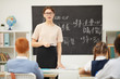 © AnnaStills - Young woman in eyeglasses working as a teacher at school and teaching the school children