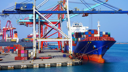 A huge container ship in the cargo terminal of an Asian port in Taiwan. Port container cranes load a moored barge with multi-colored containers. worldwide shipping by sea