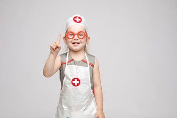 Cropped view of funny little girl wearing doctor uniform looking at camera and shoring sign of silence. Preschool child playing nurse and enjoying game on isoalted background. Concept of fun and joy.