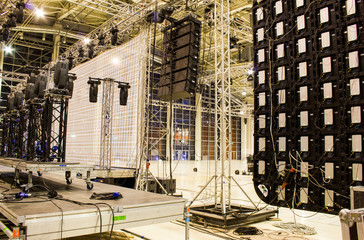 Moving head spotlight devices on a truss. Line array speakers. Big led screen. Installation of professional stage, sound, light and video equipment for a concert.