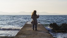 Long Shot Of A Little Girl Standing On A Dock At Rocky Seaside