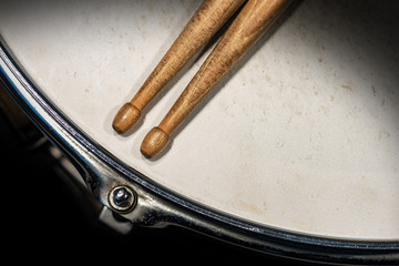 Wall Mural - Close-up of two wooden drumsticks on an old metallic snare drum with dark background. Percussion instrument