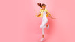 Full length portrait of a laughing woman jumping over pink background. Looking at camera. Beautiful young woman in sunglasses,white shirt,white jeans posing, jumping. Copy space.