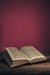Poster - Old book on a old oak wooden table and red wall background behind.