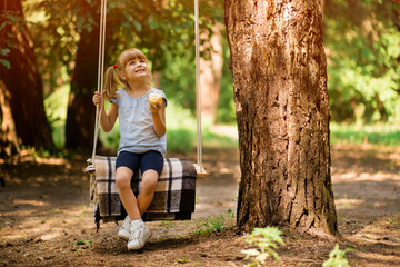 Little girl eat apple and having fun on swing outdoor in park