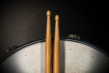 Close-up Of Two Wooden Drumsticks On An Old Metallic Snare Drum With Dark Background. Percussion Instrument
