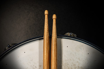 Wall Mural - Close-up of two wooden drumsticks on an old metallic snare drum with dark background. Percussion instrument