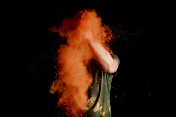 Wall Mural - woman with orange colorful holi paint explosion in front of face on black background