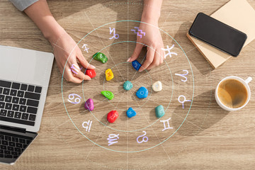 top view of astrologer holding stones with zodiac sign beside laptop, coffee illustration