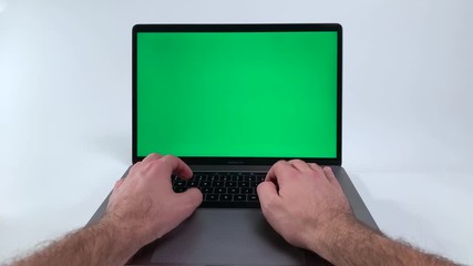 Blank Green screen on a laptop computer. Man pressing buttons on a black keyboard on a silver notebook with green color over the screen. Working on a computer with white backdrop and greenscreen.