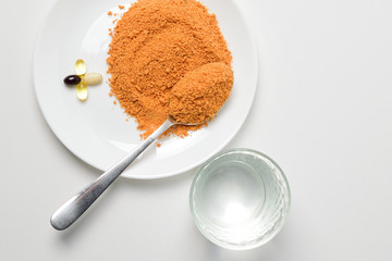 Protein soup powder on a spoon. Meal replacement. Dry soup. Multivitamins, astaxanthin, fish oil, omega pills.  Closeup.