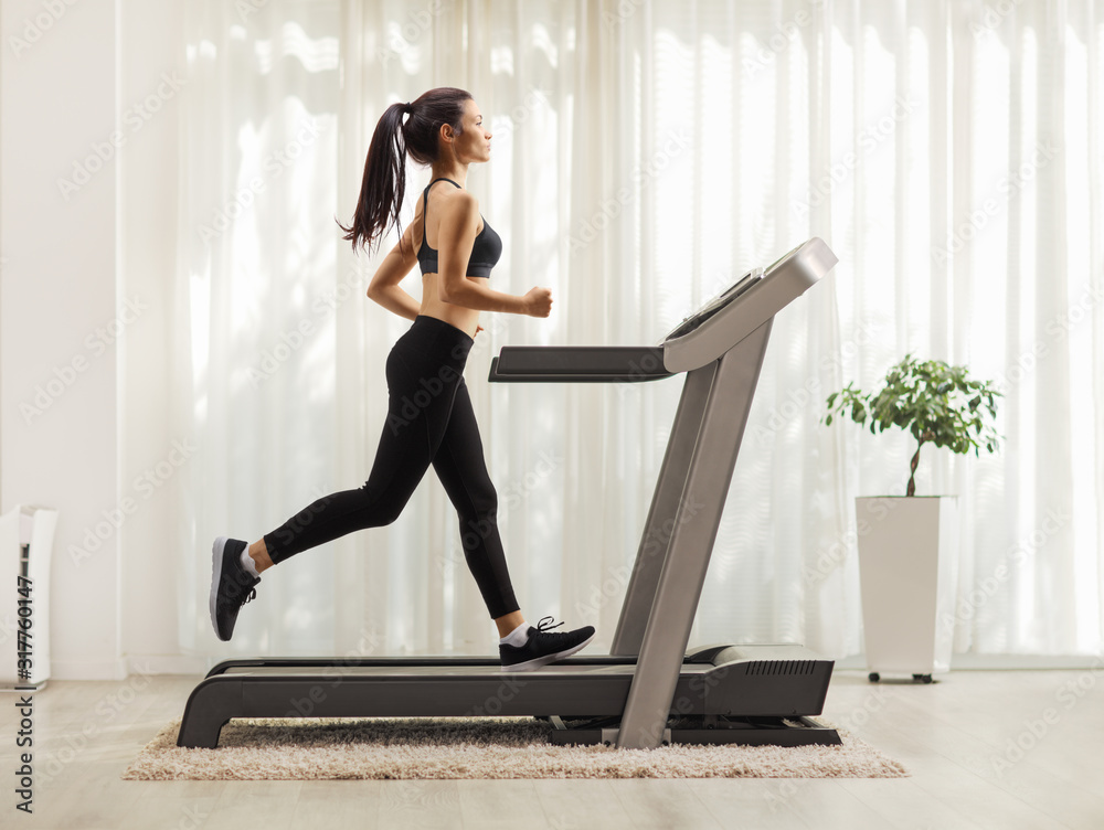 Young woman running on a treadmill indoors - obrazy, fototapety, plakaty 