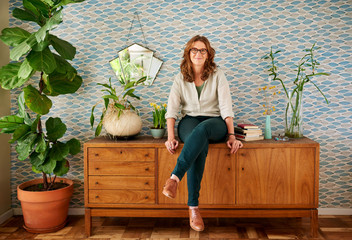 Wall Mural - Mature woman smiling while sitting on a cabinet at home