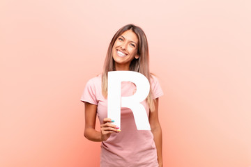 young pretty woman excited, happy, joyful, holding the letter R of the alphabet to form a word or a sentence.