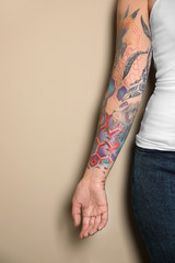 Wall Mural - Woman with colorful tattoos on arm against beige background, closeup