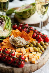 Delicious gourmet food degustation in Paris, France. Artichoke creme mousse, cheese, ripe red tomato, olives, corn chips. Two glasses of expensive white wine. Rusic wooden board, close up, front view