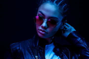 Wall Mural - portrait of an African American young woman in sunglasses isolated on a black background in neon light