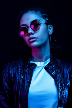 portrait of an African American young woman in sunglasses isolated on a black background in neon light