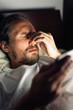 © Cavan Images - Bearded caucasian male with a headache in bed holding a tablet.