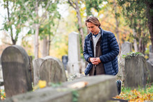 Mourning Young Man Kneeling In Front Of A Grave On A Cemetery